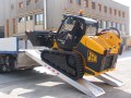 Skid steer loader driving up channel ramps 
