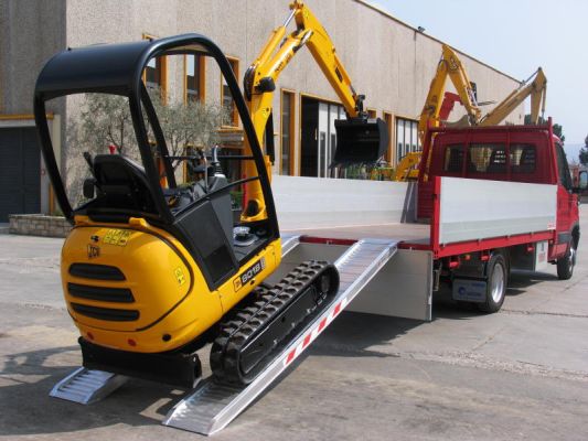 Mini digger loading in to tipper truck on loading ramps 