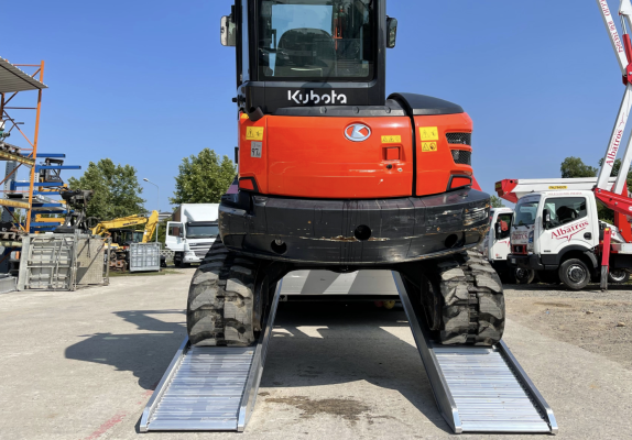 Digger driving up pair of loading ramps 