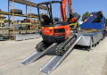 Digger driving up pair of loading ramps 
