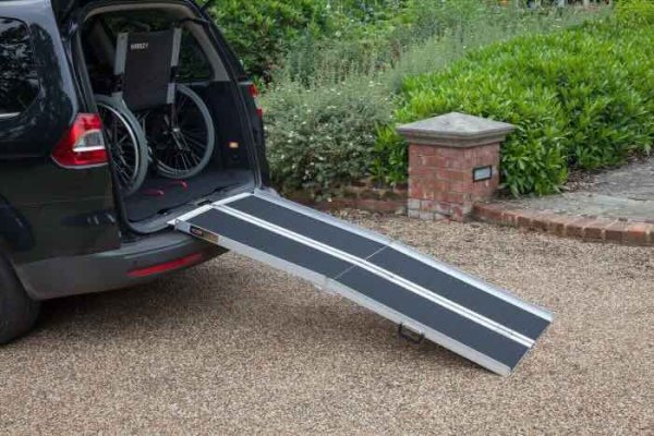Multifold mobility scooter loading ramp resting on a car boot with a wheelchair stored in car 