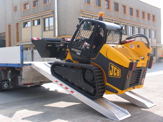 Skid steer loader driving up channel ramps 