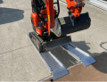 Digger driving up plant ramps resting on flat bed van