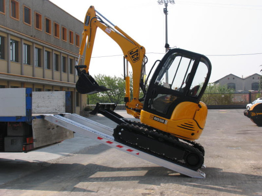 Mini digger driving up loading ramps 
