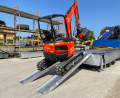 Digger driving up pair of loading ramps 