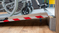 extra wide folding wheelchair ramp with red safety stripes, resting on a step with a manual wheelchair being pushed up. Side view shows the safety tape up close
