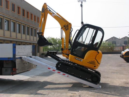 Mini digger driving on loading ramps 
