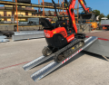 Digger driving up alloy ramps resting on flat bed van 