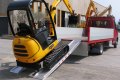 Digger driving up a pair of aluminium loading ramps onto a flat bed van
