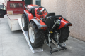 Tractor driving up vehicle ramps onto flat bed van 